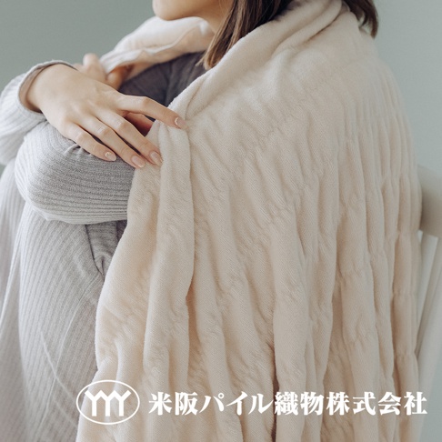 米色輕暖柔蓬抗摩四季毯，觸感柔軟，表面有菱格紋理，蓋在身穿灰色條紋衣物的女性身上。