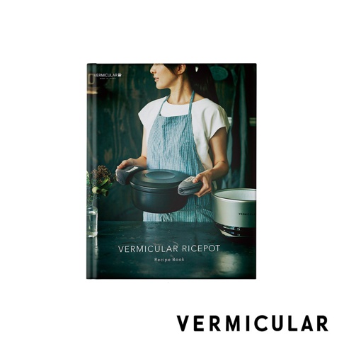 一位女性穿著藍白條紋圍裙，雙手戴著隔熱墊，拿著一個黑色IH琺瑯鑄鐵鍋。鍋子下方擺放著一個銀色電子鍋。