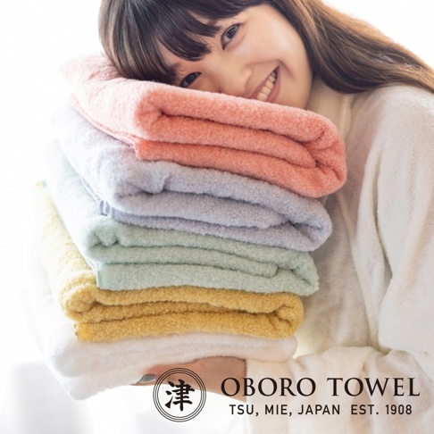 一疊五色（粉色、淺紫、淺綠、鵝黃、白色）的柔軟毛巾，質地看起來蓬鬆吸水，由一位女士抱著。