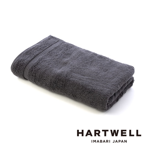 一條折疊的炭灰色今治毛巾，觸感柔軟，邊緣有精緻的線條裝飾。