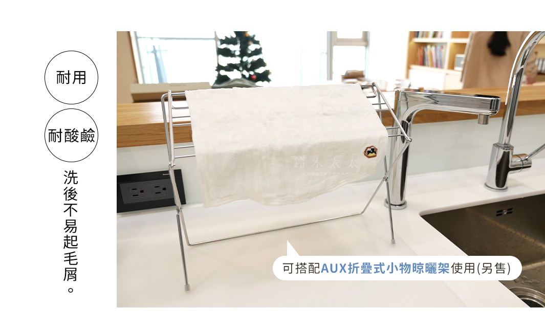 白色柔軟的八重紗擦拭巾，繡有「露木太太」字樣及小狗圖案，平鋪在銀色金屬置物架上，置物架置於廚房檯面上，背景為水龍頭及水槽。