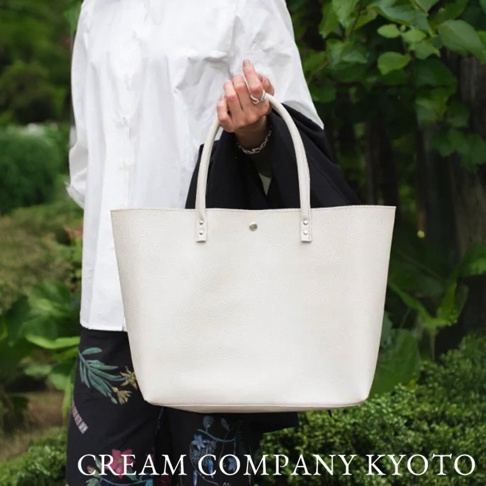 京都職人手作的米白色皮革托特包，設有兩個短手提帶和一個磁扣。包身紋理細緻，容量寬敞，設計簡約大方。