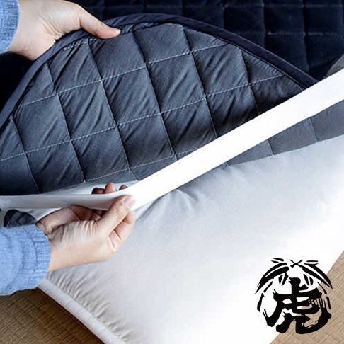 兩隻手正將深灰色菱格紋的竹炭床墊套在白色床墊上，床墊邊緣有白色固定綁帶。