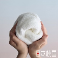 兩隻手捧著一條捲起來的白色蓬鬆毛巾，背景為淺灰色，右下角有日本桃雪的標誌和文字。