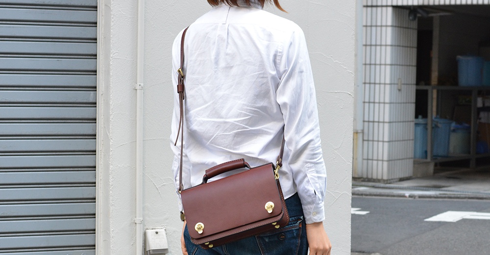 深棕色皮革手提斜背包，具備雙扣翻蓋設計，可斜揹或手提。