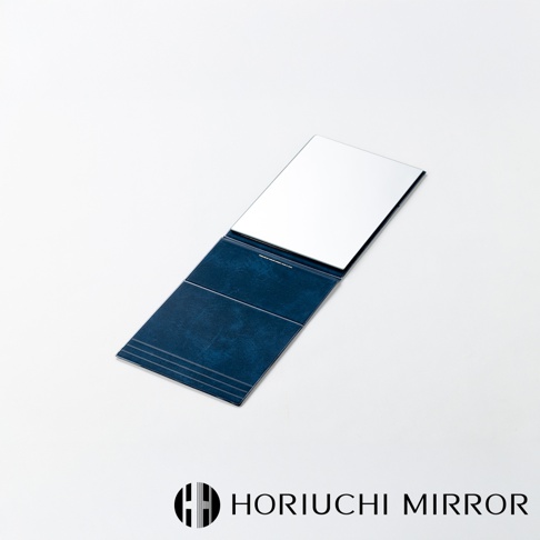 深藍色皮革材質的NAPURE桌上型2Way折疊化妝鏡，鏡面朝上，鏡蓋上印有細緻的線條紋路，整體呈現簡約質感。