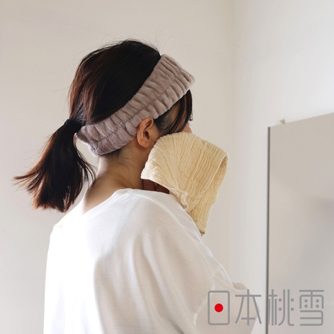 一位女子戴著淺紫色髮帶，正用米白色褶皺毛巾擦拭臉部，背景為白色牆壁，右下角有「日本桃雪」的品牌標誌。