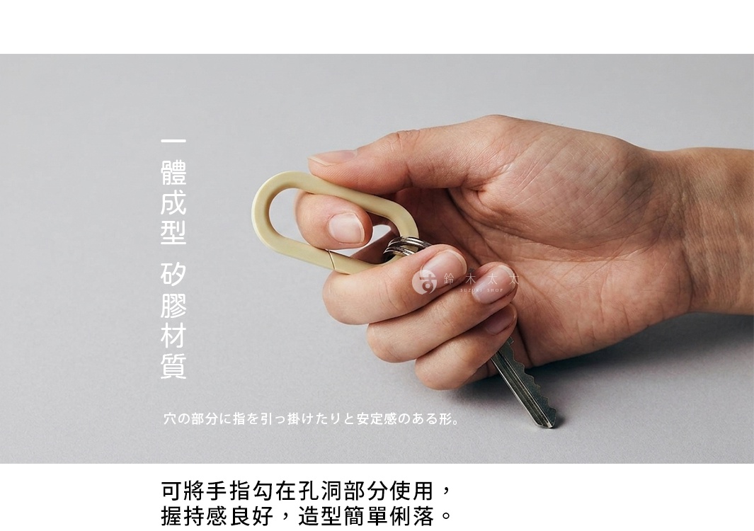 一隻手正拿著一個米色的一體成型矽膠橢圓形鑰匙圈，該鑰匙圈連接著金屬鑰匙，產品特色強調其孔洞設計方便手指勾掛，且材質具備良好的握持感與簡約俐落的造型。