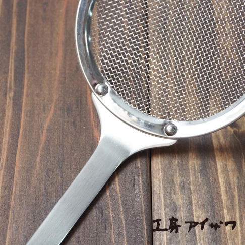 不鏽鋼萬用撈油勺，勺頭為細網篩，邊緣和手柄為銀色不鏽鋼材質，手柄呈扁平狀，與勺頭連接處有兩個鉚釘固定。