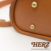 皮革立體商務後背包，採用鞣製皮革材質，呈現自然的棕褐色調，配有兩個黃銅色鉚釘裝飾，並可見一條皮革背帶。