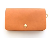 棕色皮革製成的旅行長夾，正面中央有一個金色按扣，右側有一個金色 D 型環。