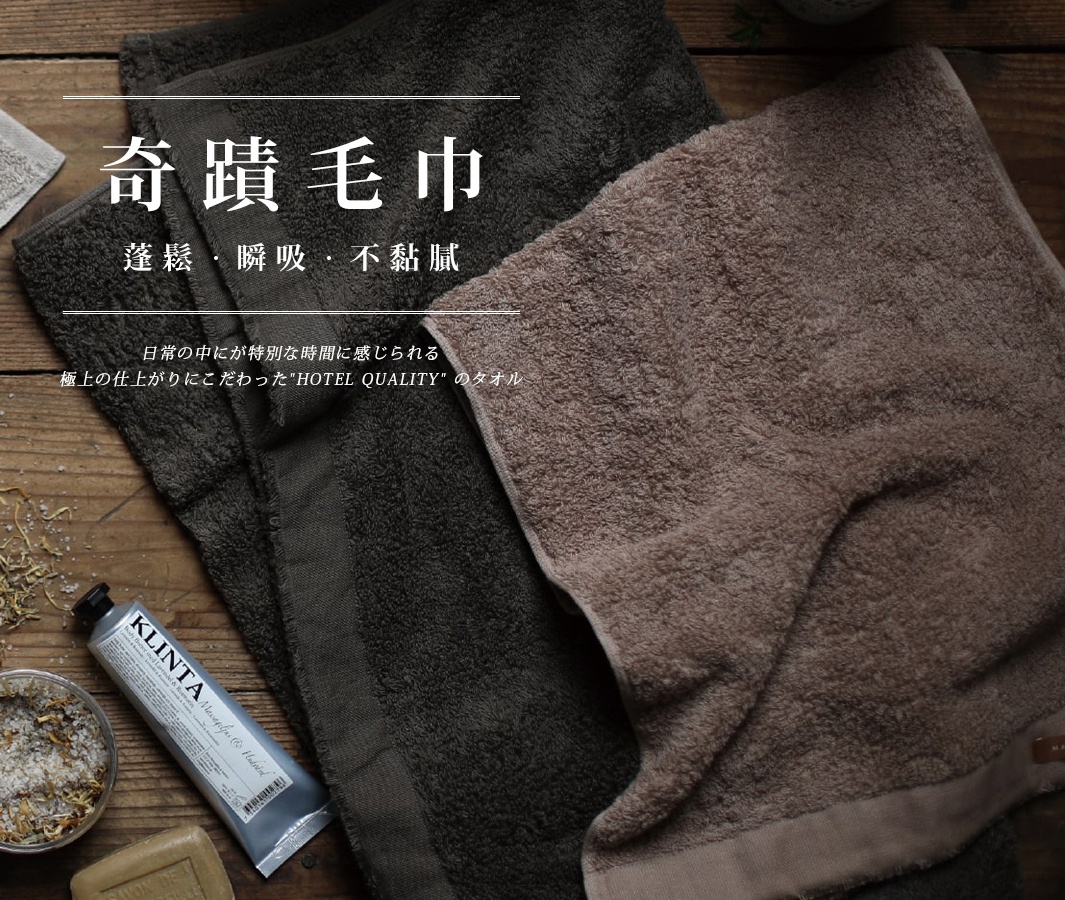 兩條泉州匹馬棉浴巾，一條為深灰色，另一條為淺棕色，材質柔軟蓬鬆，置於木紋背景上。