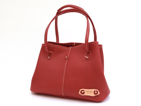 紅色皮革托特包，包身縫線明顯，配有兩個可調式提把，包側下方有一個皮革品牌標籤。