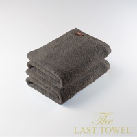 深棕色純棉柔浴巾堆疊，頂部一條繡有品牌標籤，質感厚實，整體呈暖色調。