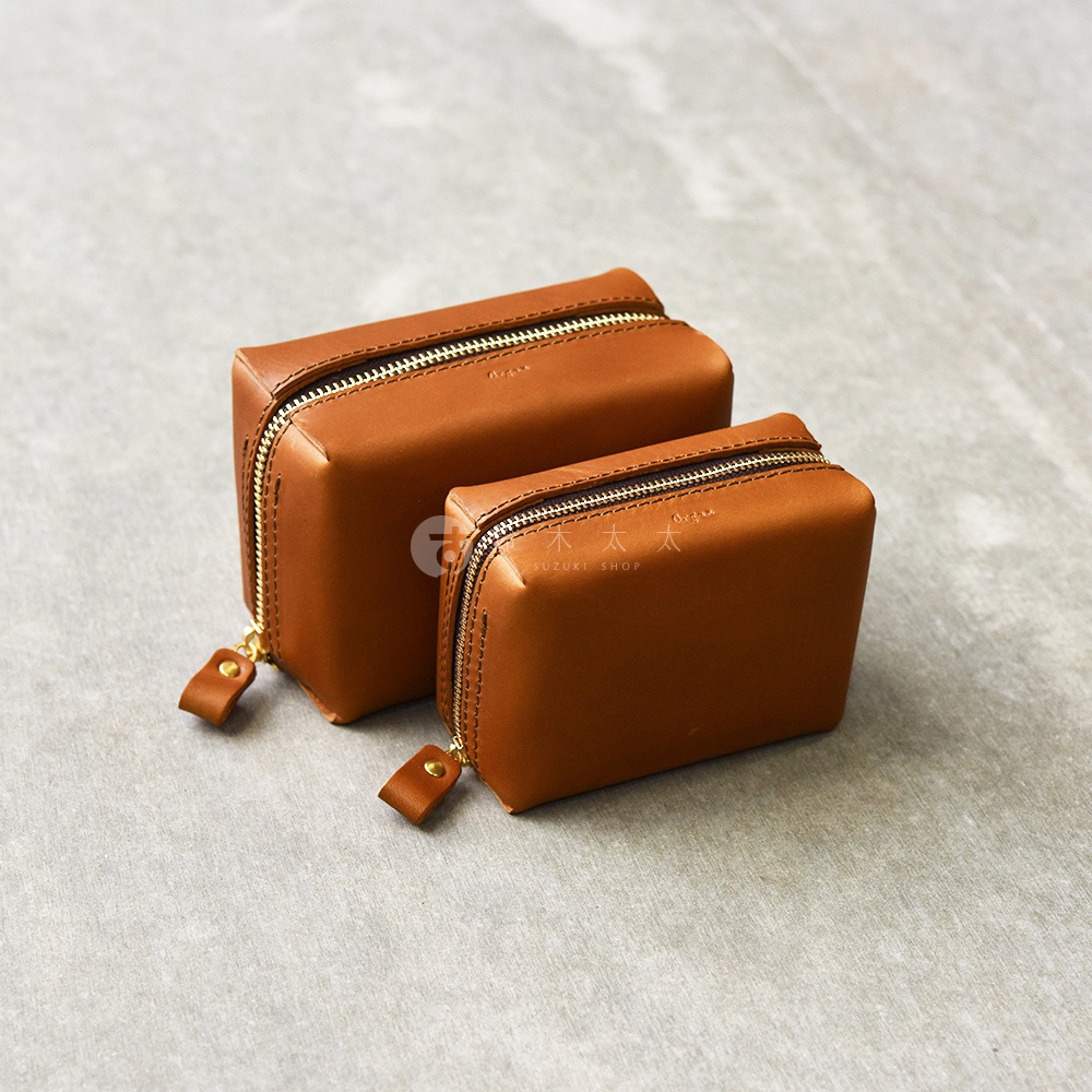 兩個不同尺寸的棕色皮革箱型收納包，配有金色拉鍊和皮革拉環，擺放在淺灰色背景上