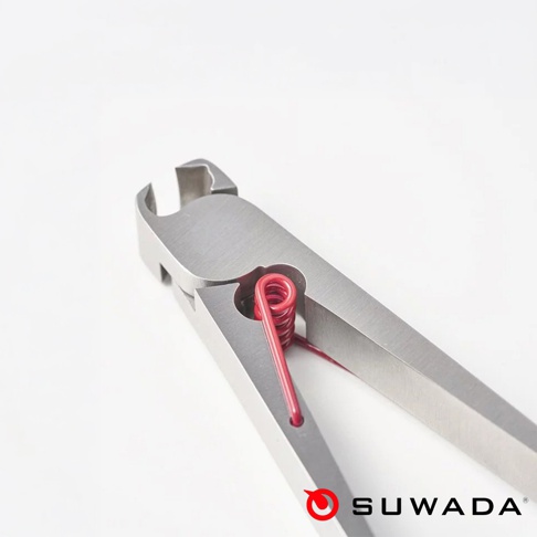 這是一張特寫鏡頭，展示了SUWADA波堤指甲剪的頂部細節，銀色金屬刀口經過精密加工，中央處嵌入了一個亮紅色的螺旋彈簧，整體設計簡潔洗鍊，右下角印有SUWADA品牌名稱與標誌。