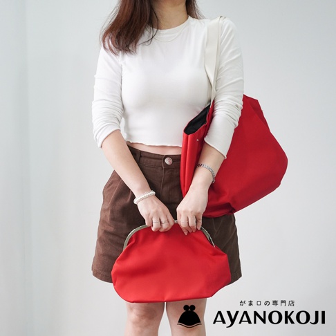 一位身穿白色長袖上衣和棕色短褲的女子，手裡拿著一個紅色的口金包，左肩斜挎一個紅色的托特包。