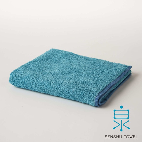 SOLID 細柔蓬韌緞澤長纖毛巾，此款為水藍色，質地蓬鬆，織紋細緻，邊緣有深藍色滾邊，右下角有「泉」字 Logo 及「SENSHU TOWEL」字樣。