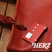 日本HERZ品牌紅皮革，特寫展示皮革材質、手縫針線細節、金屬扣件，以及標誌性的「HERZ HAND MADE IN JAPAN Since1973」字樣。
