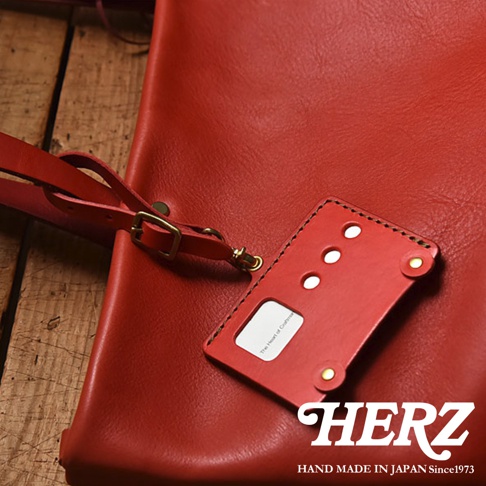 日本HERZ品牌紅皮革，特寫展示皮革材質、手縫針線細節、金屬扣件，以及標誌性的「HERZ HAND MADE IN JAPAN Since1973」字樣。