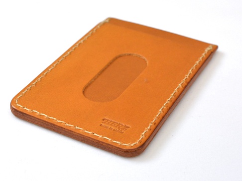 職人手作皮革直式票券收納夾，淺棕色皮革，表面有橢圓形開口，車縫線為米白色，角落有品牌標誌。