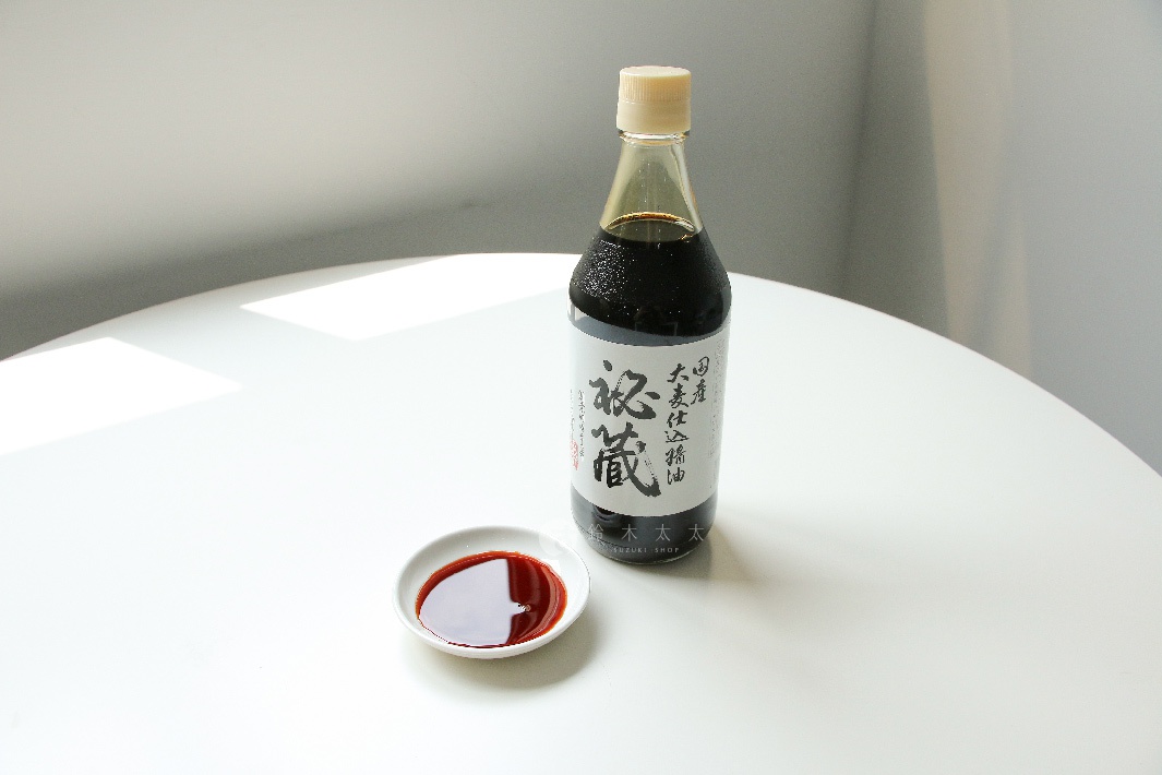 玻璃瓶裝的秘藏醬油，瓶身貼有黑色字體的中文標籤，醬油呈深褐色，旁邊有一個白色碟子，碟中盛有少量醬油。