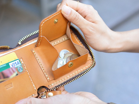 棕褐色皮革拉鍊短夾，內有卡槽、零錢袋，裝有信用卡及日圓硬幣，手工縫線清晰可見，拉鍊為金屬材質。