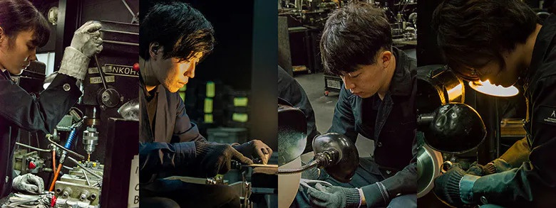 四位諏訪田製作所的職人正專注於工作台前進行指甲剪的精密加工，畫面展示了從機械鑽孔到細節打磨的手工生產過程，職人們配戴工作手套並在局部照明下精細修整金屬零件。