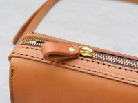 淺棕色皮革拉鍊單肩包的特寫，展示了黃銅拉鍊、皮革拉片和縫線細節。