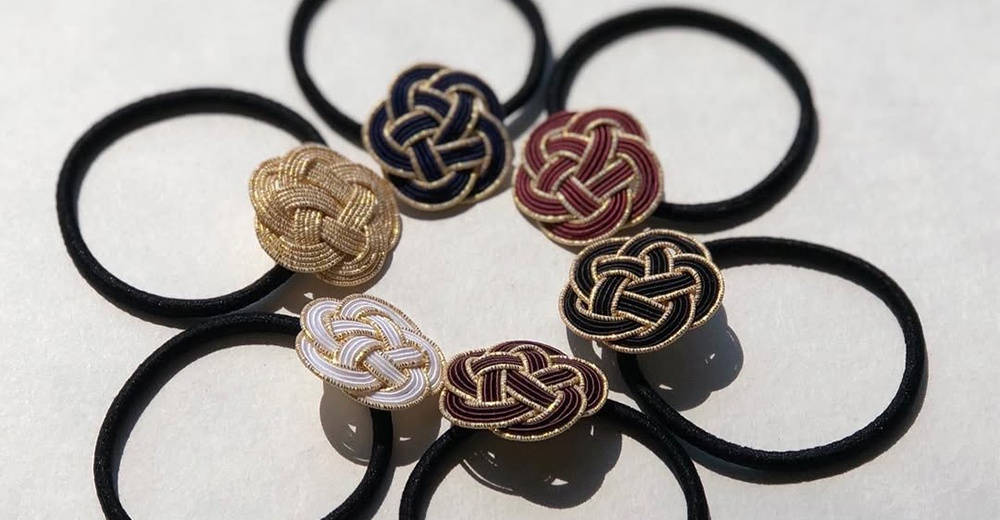 一組包含金絲水引花結裝飾的黑色髮圈，花結有金、深藍、酒紅、黑白與酒紅金邊等顏色，呈現傳統日式編織工藝。