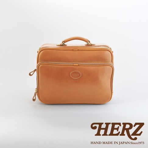 職人手作皮革兩用商務公事包，呈現自然光澤的棕褐色皮革，設有頂部提把、雙拉鍊主隔層及前置拉鍊口袋，風格簡潔實用。