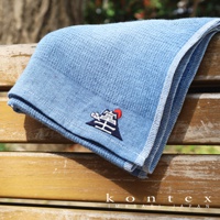 淺藍色長毛巾，輕薄材質，表面有細緻的格子紋路，一角繡有富士山圖案，搭配紅色太陽和白色雲霧。