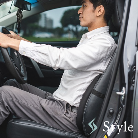 一位男士坐在汽車駕駛座上，使用黑色皮革材質、帶有黑色綁帶的腰部支撐靠墊，提供背部支撐。