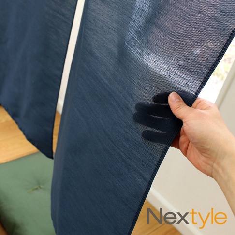 深藍色手作門簾，細緻織紋，半透明材質，邊緣縫線清晰，展示於窗邊，搭配木質地板和綠色坐墊。