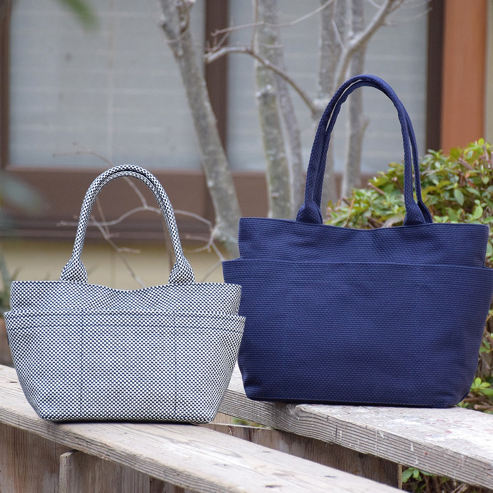兩款三河木綿刺子織手提托特包，左為黑白棋盤格紋，右為深藍色，皆有堅固的編織提把及前後口袋設計。