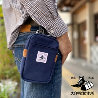 深藍色石洗帆布斜背手機包，配有棕色皮革裝飾和品牌標籤，可掛在牛仔褲上。