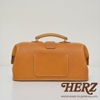 職人手作皮革長型迷你醫生包，採用天然皮革材質，呈現溫潤的焦糖棕色。包款設計經典，擁有頂部提把、金屬釦環與前置方形皮夾層，整體線條簡潔，展現手工的細緻與質感。