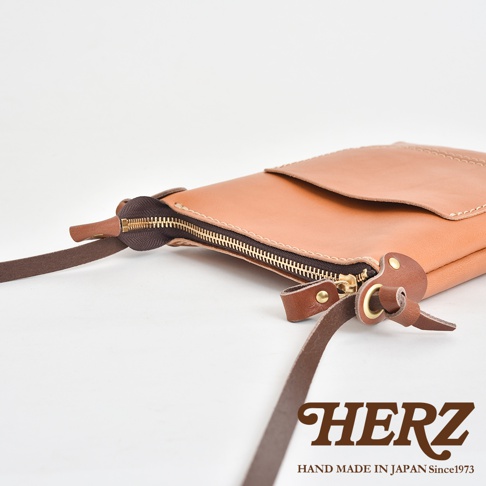職人手作皮革直式隨身單肩包，淺棕色皮革，設有拉鍊開合及可調節肩帶，金色拉鍊與銅色鈕扣點綴。