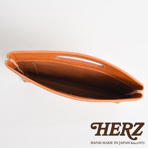 俯視角度拍攝的日本HERZ職人手作皮革收納袋，展示其淺棕色皮革材質與內部縫線細節，袋口處設有皮革手提挖孔設計，整體呈現極簡且耐用的工藝風格。