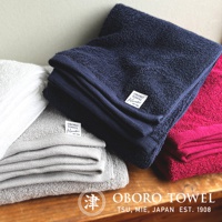 白色、灰色、深藍色及桃紅色的細纖浴巾堆疊展示，質感柔軟。