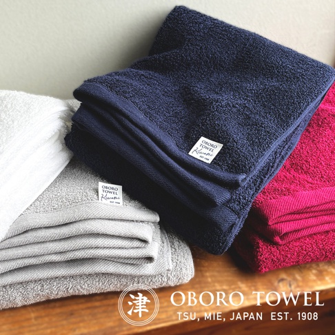 白色、灰色、深藍色及桃紅色的細纖浴巾堆疊展示，質感柔軟。