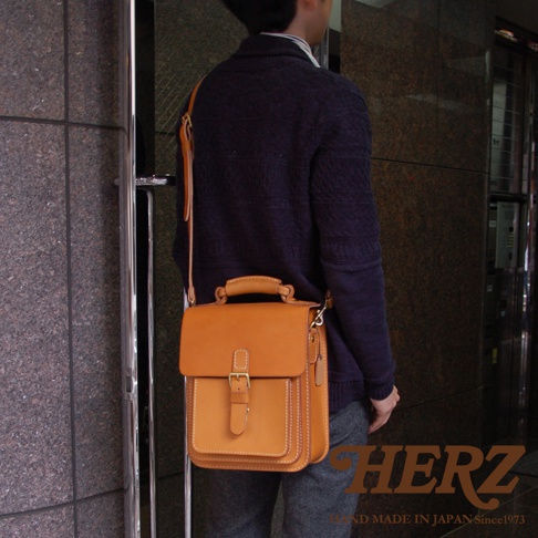 棕色皮革職人手作單肩兩用小方包，有頂部提把、翻蓋式開口及金屬扣環，以側背方式展示。