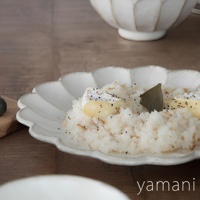 一個白色、帶有六瓣花型邊緣的陶瓷主食盤，盤中盛有白飯、起司塊、香料和一片葉子。