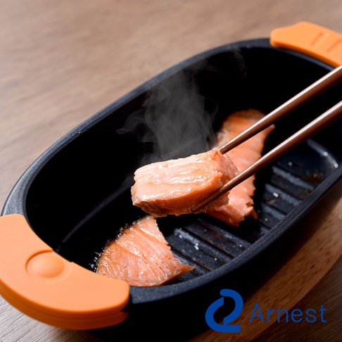 一塊烹煮中的鮭魚由筷子夾起，上方冒著熱氣，置於Arnest的多功能快速微波料理器中。