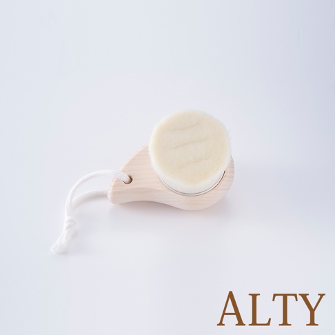 淺木色手柄的洗臉刷，圓形刷頭為米白色絨毛材質，帶有白色編織掛繩。