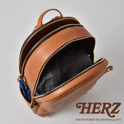 棕色皮革多功能後背包 R-21，主隔層敞開，露出內部黑色的收納袋。側面有一個小口袋，裝有藍色圖案的物品。背包配有金色拉鍊和皮革提把。