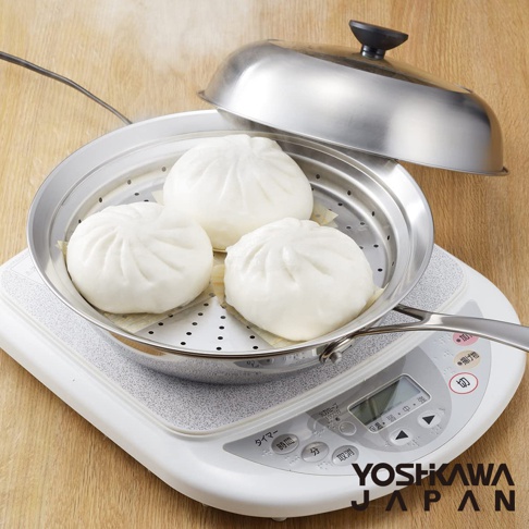 不鏽鋼蒸鍋盤置於電磁爐上，盤內有三個白色包子，蒸鍋配有透明蓋，盤身及鍋蓋材質為不鏽鋼。