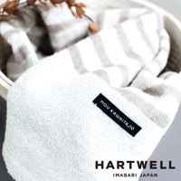 今治毛巾，白色搭配淺棕色條紋，材質柔軟，繡有「MOU KAWAITA」字樣的黑色標籤，上方有乾燥的裝飾性枝葉。