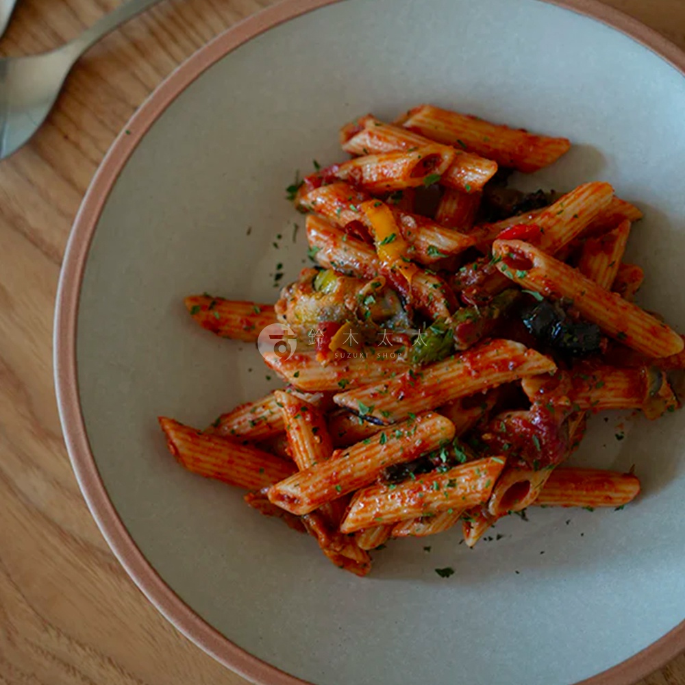 素燒百搭陶瓷義大利麵盤，盤子為淺灰色，邊緣帶有淡粉色滾邊，盛裝著滿滿的筆管麵，麵體裹滿紅醬，搭配蔬菜丁與香料。