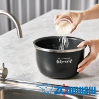 黑色金屬內鍋，內側有水位刻度，外側印有日文品牌標誌。一隻手正將米從透明容器中倒入內鍋。